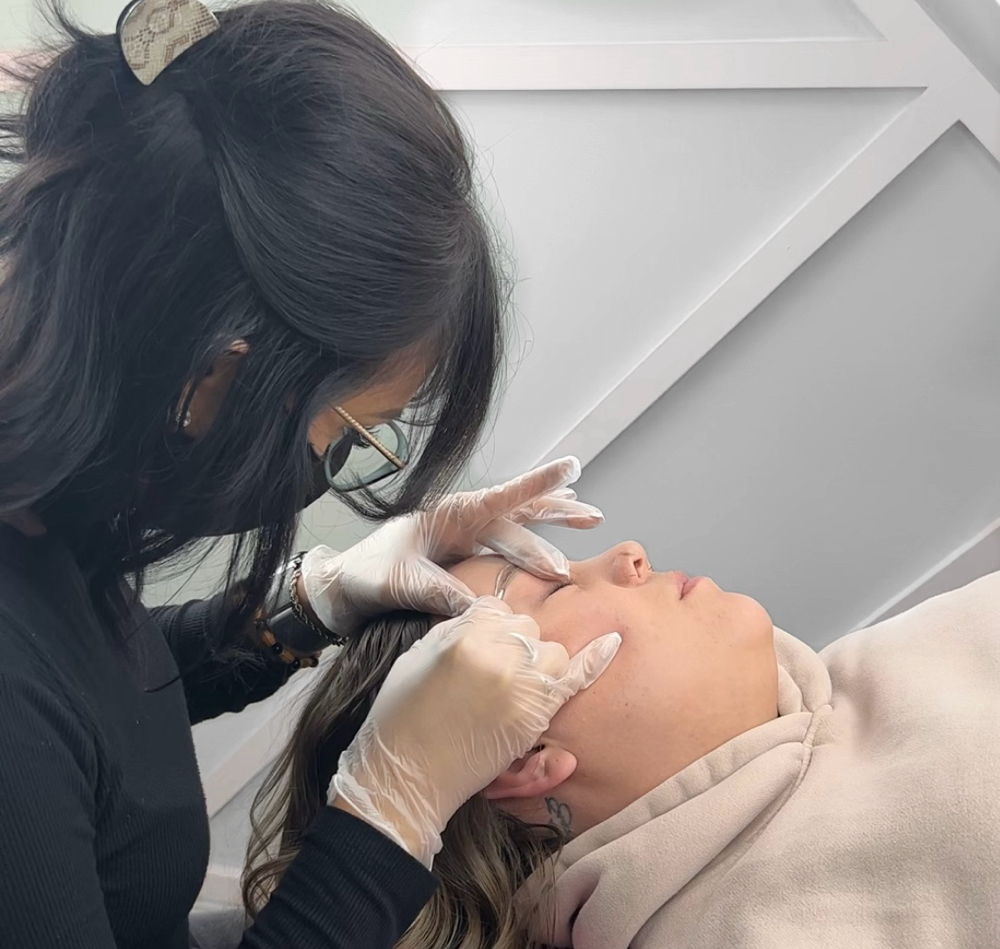 A woman laying down, getting her eyebrows permanently tattooed.