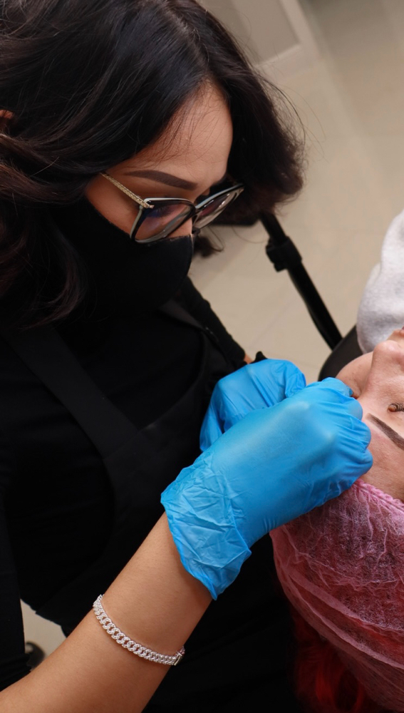 A woman laying down, getting her eyebrows permanently tattooed.