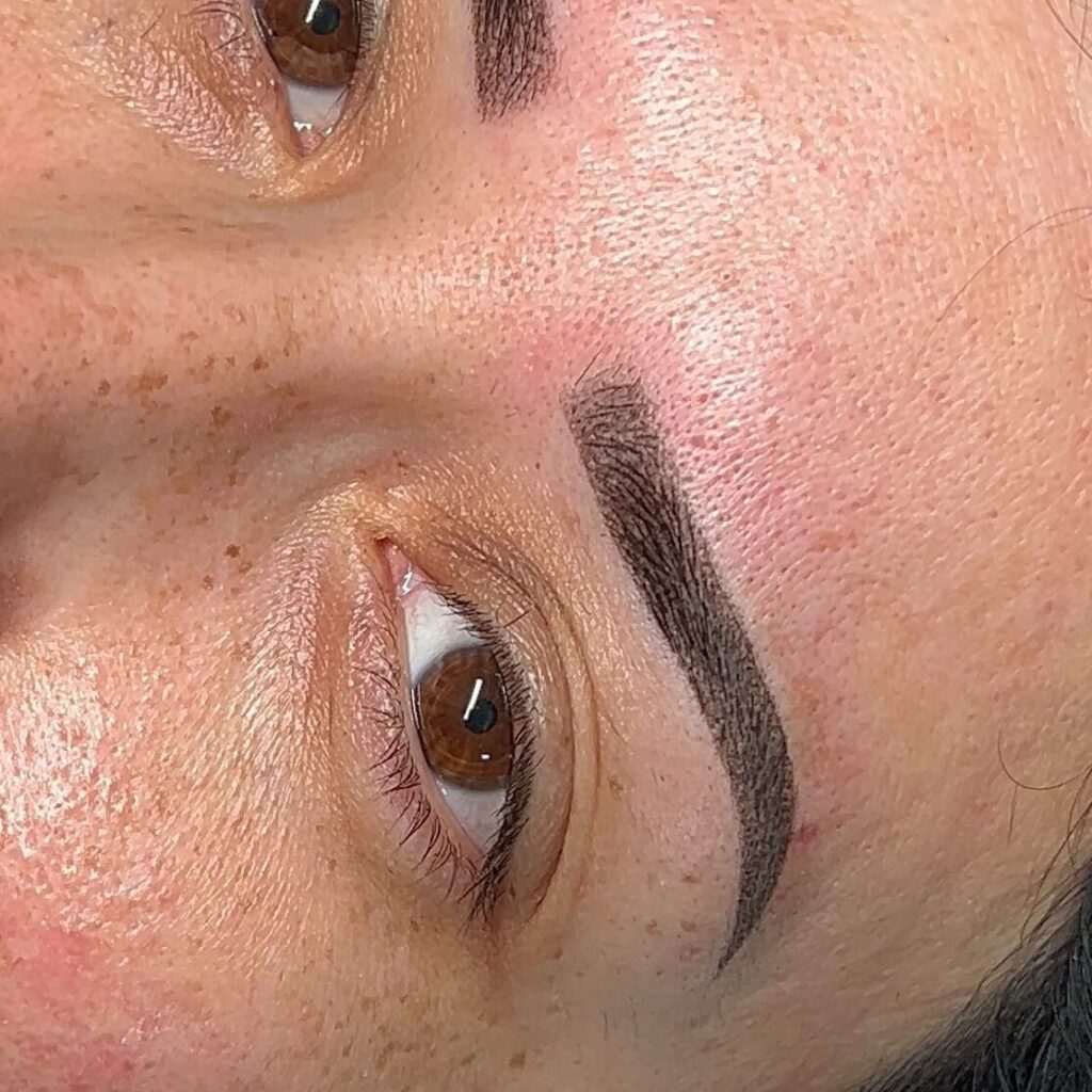 A woman laying down, showing off her newly done brow tattoo.