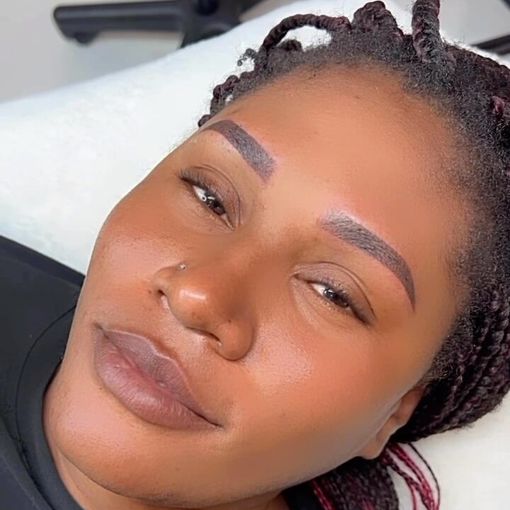 A woman laying down, showing off her newly done brow tattoo.