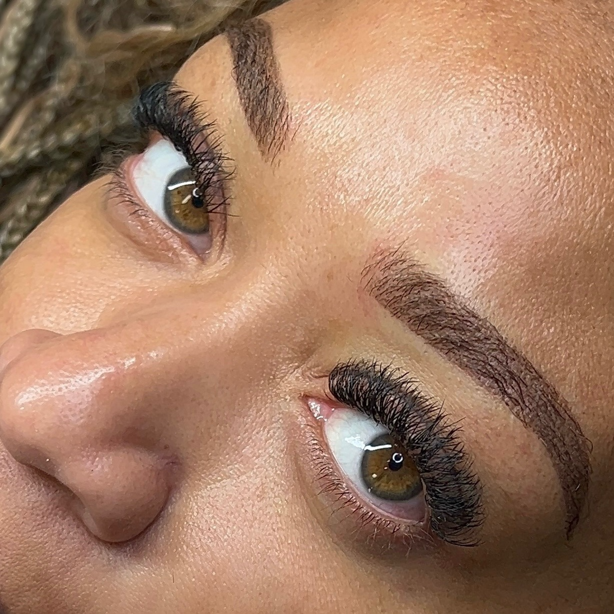 A woman laying down, looking into the camera, showing off her newly done ombre brow tattoo.
