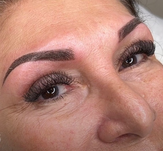 A woman laying down, looking into the camera, showing off her newly done powder brow tattoo.