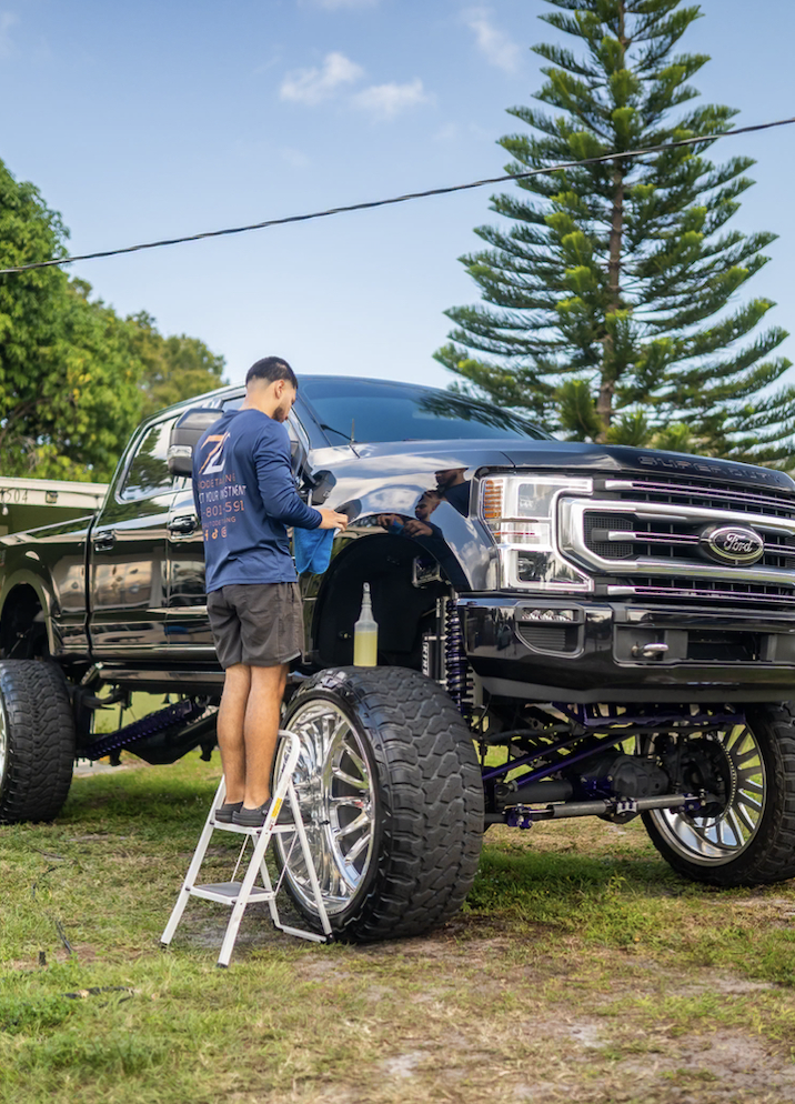 Owner of ZC Auto Detailing, on a step ladder as he details a large truck.