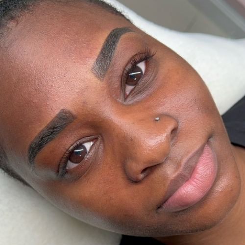 A woman laying down, showing off her newly done brow tattoo.
