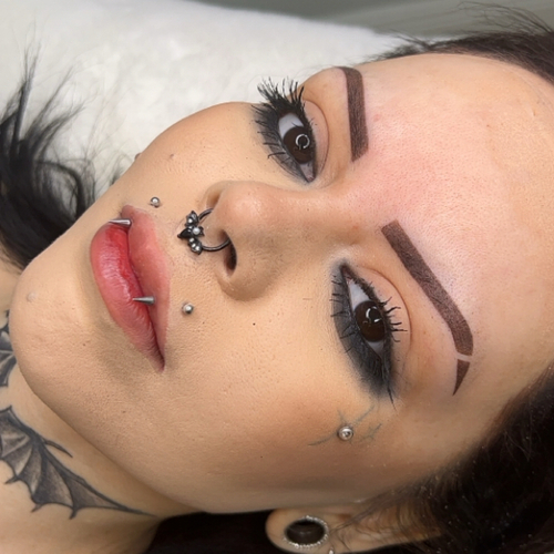 A woman laying down, showing off her newly done brow tattoo.