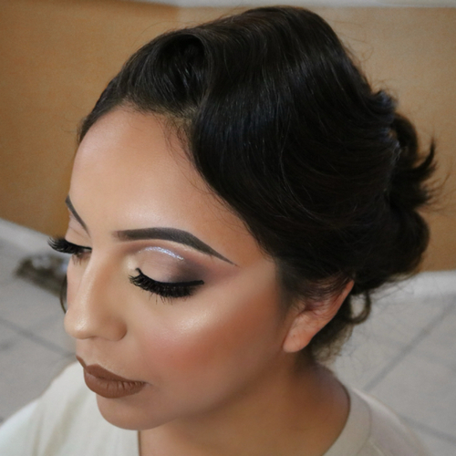 A woman sitting down, showing off her newly done wedding makeup.