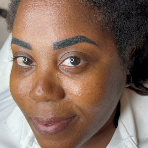 A woman laying down, showing off her newly done brow tattoo.