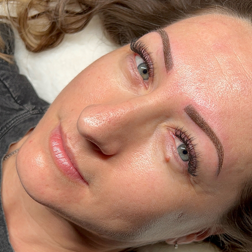 A woman laying down, showing off her newly done brow tattoo.