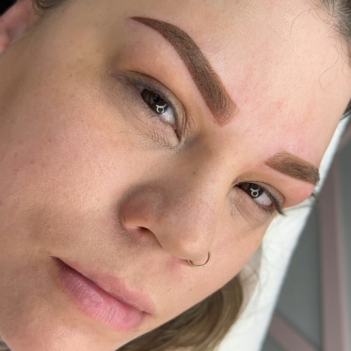 A woman staring into the camera, showing off her newly done tattooed brows.