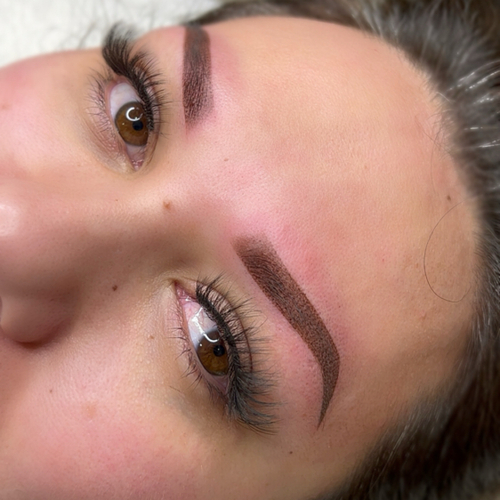 A woman laying down, showing off her newly done brow tattoo.