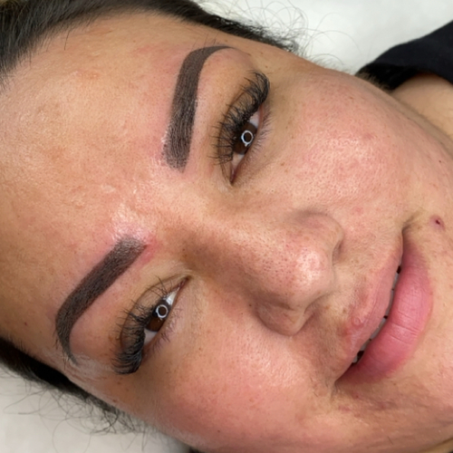 A woman laying down, showing off her newly done brow tattoo.