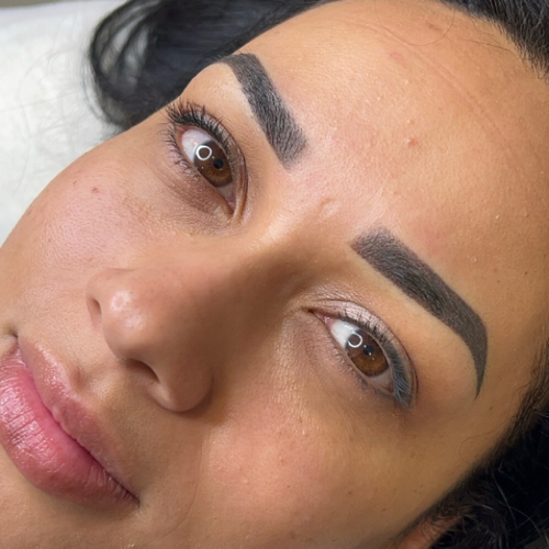 A woman laying down, showing off her newly done brow tattoo.