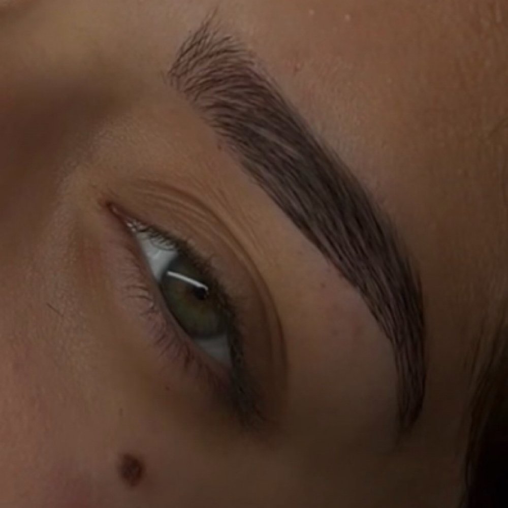 A woman laying down, getting her eyebrows permanently tattooed.